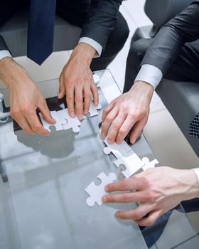 close up.business people putting together a puzzle ,sitting behind a Desk.the concept of cooperation