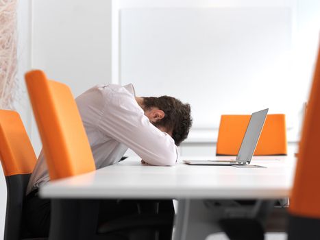 Frustrated young business man have stress problems. Sitting alone at office meeting room  and working on laptop compute.