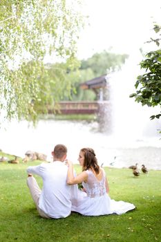 Handsome groom and fiancee sitting near lake and resting. Concept of married couple and nature.