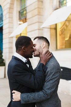 Afro american gay kissing caucasian boy outside, wearing suits. Concept of lgbt and same sex couple.