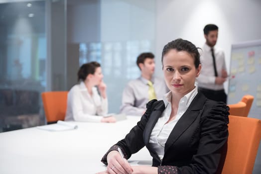 young business woman on meeting usineg laptop computer, blured group of people in background at  modern bright startup office interior taking notes on white flip board and brainstorming about plans and ideas