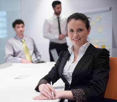 young business woman on meeting usineg laptop computer, blured group of people in background at  modern bright startup office interior taking notes on white flip board and brainstorming about plans and ideas