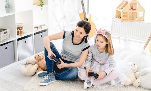 Cute little girl playing video game with mother in playroom