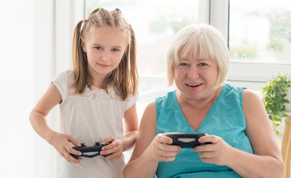 Happy aged woman playing video game with granddaughter