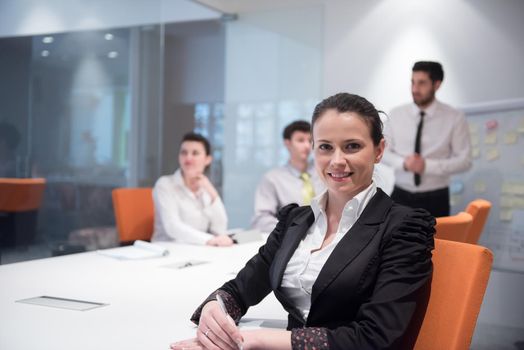 young business woman on meeting usineg laptop computer, blured group of people in background at  modern bright startup office interior taking notes on white flip board and brainstorming about plans and ideas