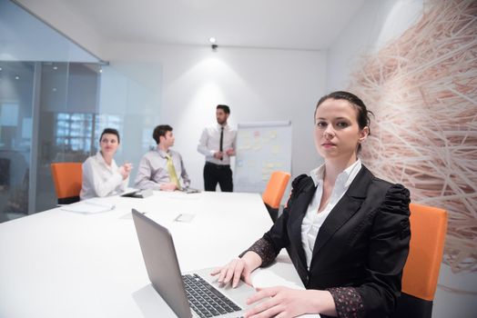 young business woman on meeting usineg laptop computer, blured group of people in background at  modern bright startup office interior taking notes on white flip board and brainstorming about plans and ideas