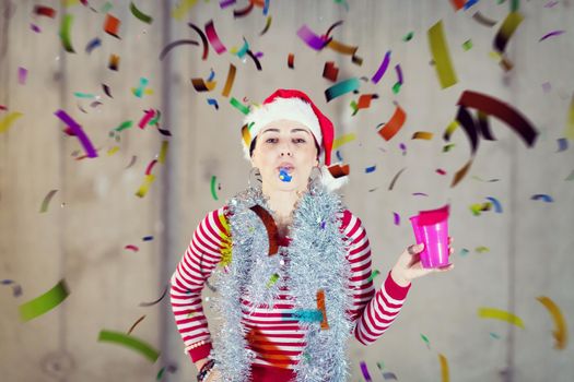 young happy casual business woman wearing a red hat and blowing party whistle while having new years confetti party in front of concrete wall