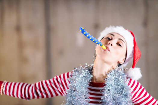 young happy casual business woman wearing a red hat and blowing party whistle while dancing during new years party in front of concrete wall