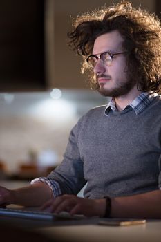 Young man working on computer at night in dark office. The designer works in the later time.