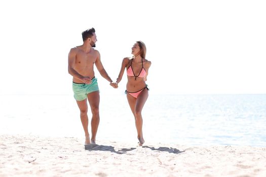Honeymoon couple holding hand walking on beautiful white sand beach in summer.