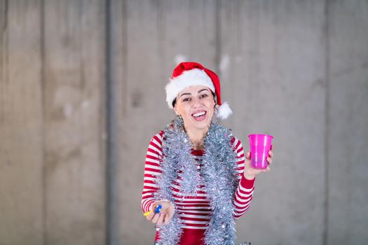 young happy casual business woman wearing a red hat and blowing party whistle while dancing during new years party in front of concrete wall