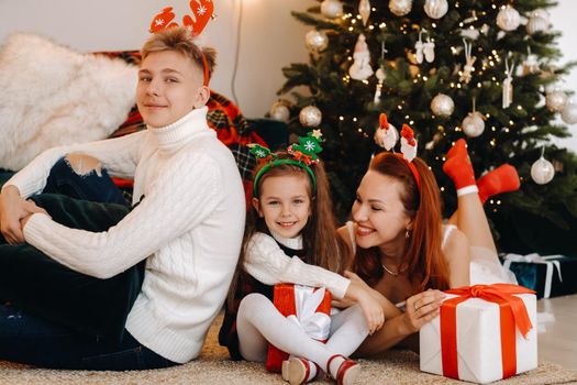 a happy family is lying on the floor of the house with New Year's gifts, next to the Christmas tree,