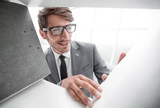 A young businessman with glasses chooses a folder for documents on the shelf