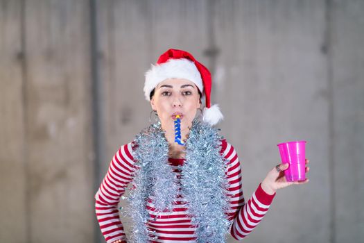 young happy casual business woman wearing a red hat and blowing party whistle while dancing during new years party in front of concrete wall