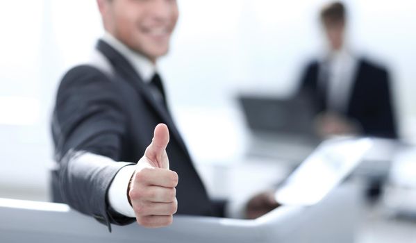 businessman on blurred background shows thumbs up while sitting in office