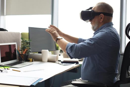Mature businessman wearing a VR headset while sitting in modern office. Change the way you see and experience the world