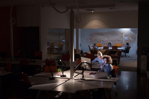 Two young designers are working on a new project in the night office using modern technology