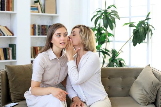 Happy middle aged mother and daughter talking on sofa in living room