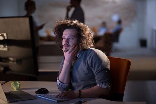 Young man working on computer at night in dark office. The designer works in the later time.