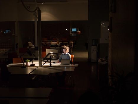 Young man working on computer at night in dark office. The designer works in the later time.