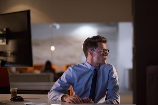 Young man working on computer at night in dark office. The designer works in the later time.