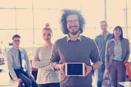 Portrait of a young businessman holding tablet in bright office with colleagues in the background