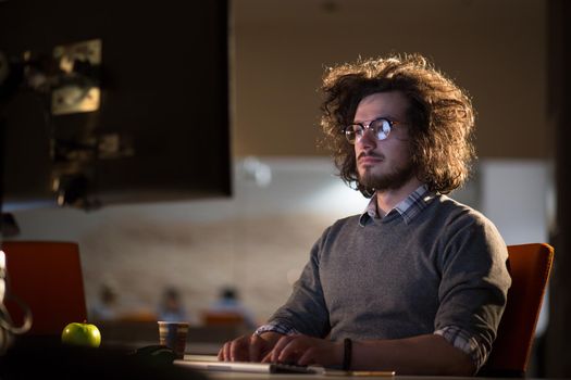 Young man working on computer at night in dark office. The designer works in the later time.