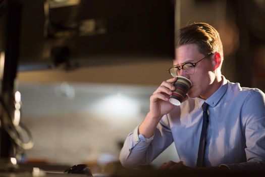 Tired businessman working late doing overtime in office at night drinking coffee to go on.