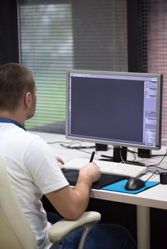 creative worker, photo editor working on graphic tablet at his desktop computer at small startup office