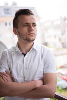 young elegant fashion man standing at balcony with arms crossed and smiling