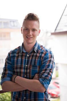 young elegant fashion man standing at balcony with arms crossed and smiling