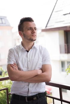 young elegant fashion man standing at balcony with arms crossed and smiling