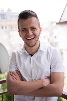 young elegant fashion man standing at balcony with arms crossed and smiling