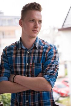 young elegant fashion man standing at balcony with arms crossed and smiling