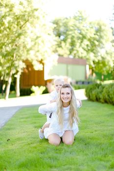 Young caucasian mother sitting with little child on grass in yard. Concept of motherhood and summer vacations.