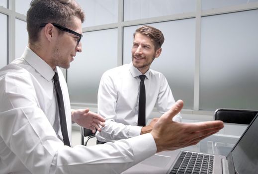 young colleagues sit at the desk in the office and work on laptops