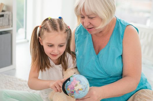 Cute grandmother and granddaughter examining globe in children's room