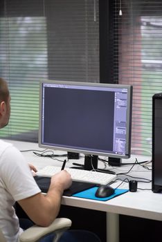 creative worker, photo editor working on graphic tablet at his desktop computer at small startup office