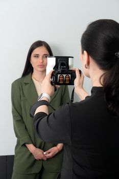 Doctor taking picture of young female patient before aesthetic treatment on white background with 3d camera system