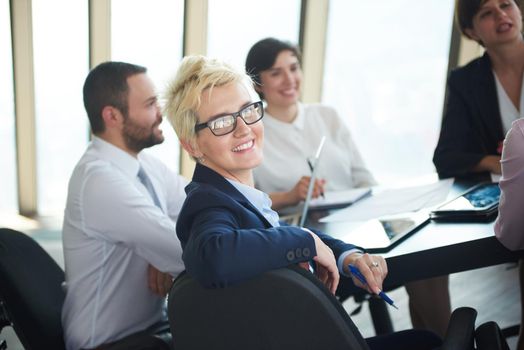 blonde with short hairstyle  and glasses,  business woman on meeting, people group in background at modern bright office indoors