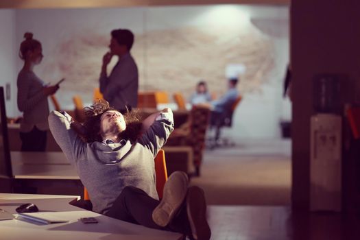 Full length of a relaxed casual young businessman sitting with legs on desk at night office