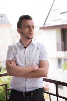 young elegant fashion man standing at balcony with arms crossed and smiling