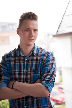 young elegant fashion man standing at balcony with arms crossed and smiling