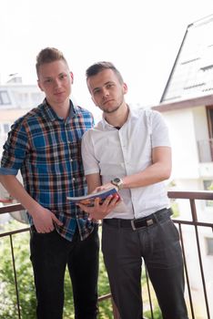 two young elegant fashion man standing at balcony and reading magazine