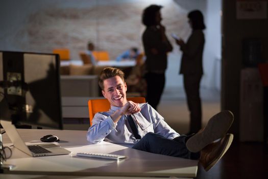 Full length of a relaxed casual young businessman sitting with legs on desk at night office