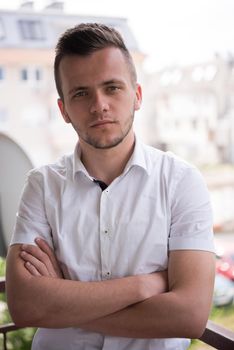 young elegant fashion man standing at balcony with arms crossed and smiling