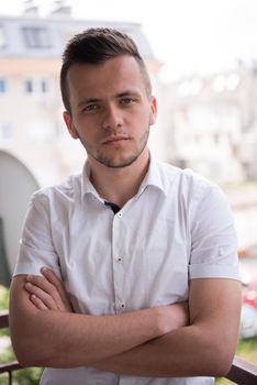 young elegant fashion man standing at balcony with arms crossed and smiling