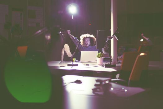 Full length of a relaxed casual young businessman sitting with legs on desk at night office