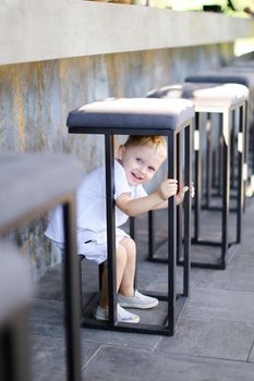 Little european male baby wearing white clothes and playing outside at street cafe. Concept of childhood.
