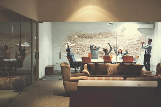 Group of young business people throwing documents and looking happy while celebrating success at their working places in night office